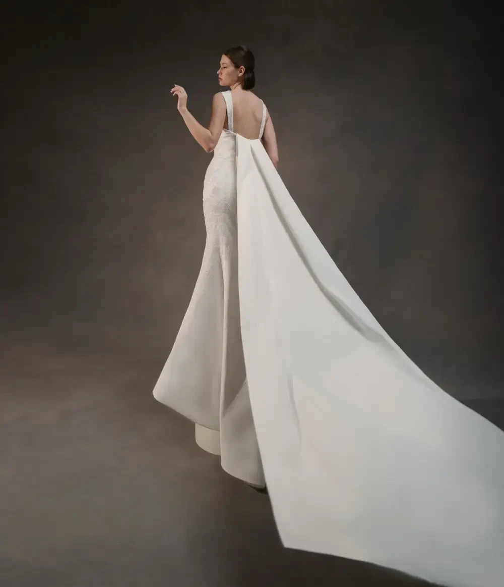 A woman wearing a sleek white gown with a long train, standing gracefully with her back to the camera.